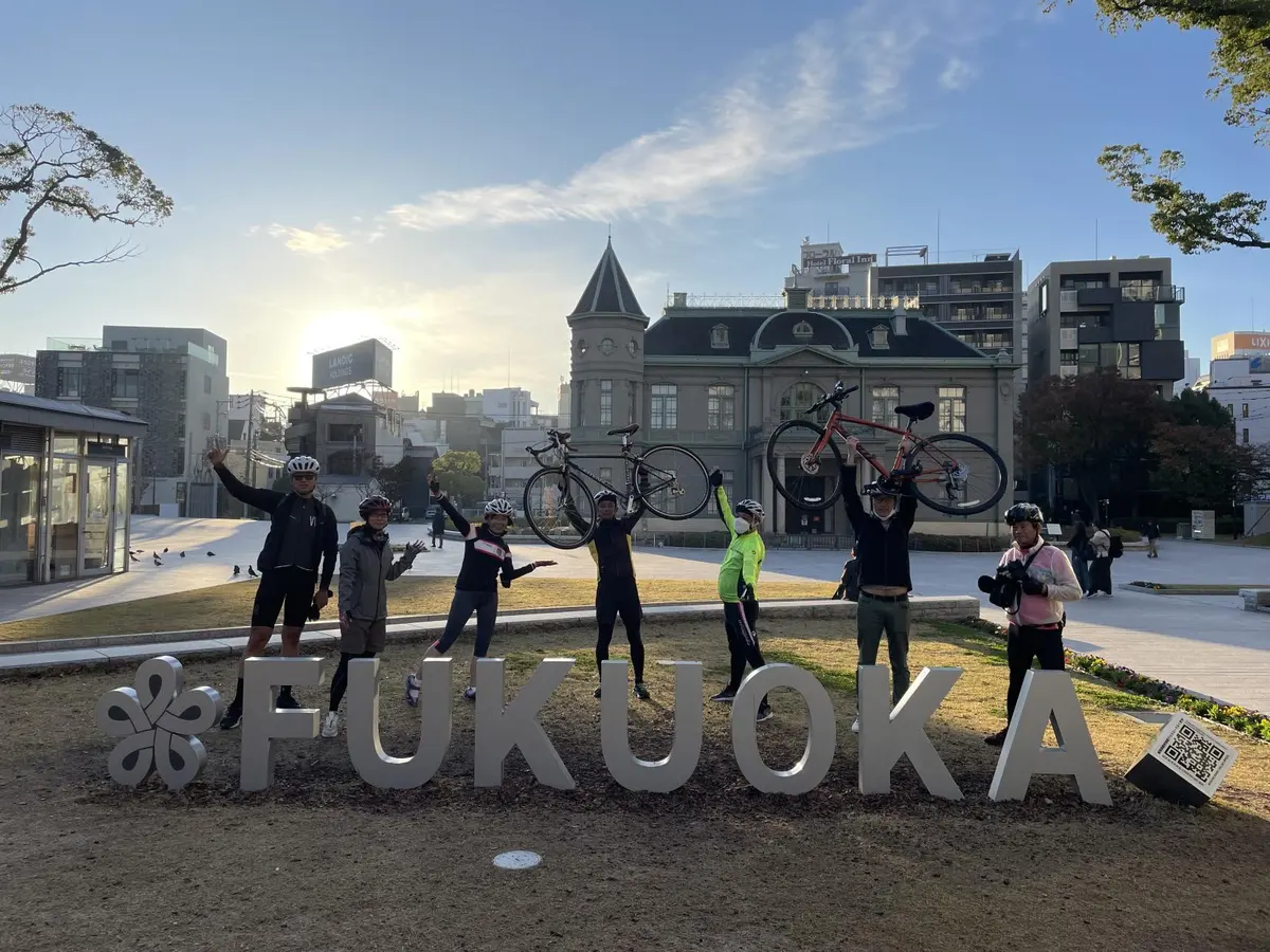 FUKUOKAモニュメント前で自転車を掲げる参加者たち